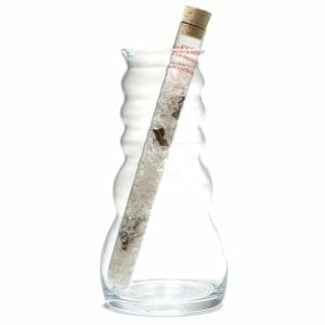 A transparent vase holds a thin, tall, corked glass bottle filled with the Пръчица за пречистване на вода със скъпоценни камъни "Спокойствие," enhancing the room's атмосфера на спокойствие.