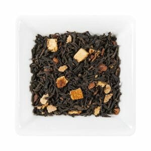 Едър план на квадратна бяла чиния, пълна с насипни листа черен чай, портокалова кора и малки парченца Ориенталски Подправки.