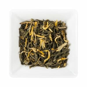 Бяла квадратна купа, пълна с насипни листа от зелен чай, смесени с жълти цветни листенца и нотка на Праскова, погледнато отгоре.