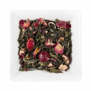 Бяла квадратна чиния, пълна със сушени листа от зелен чай, сушени розови листенца и живи Нар плодове.