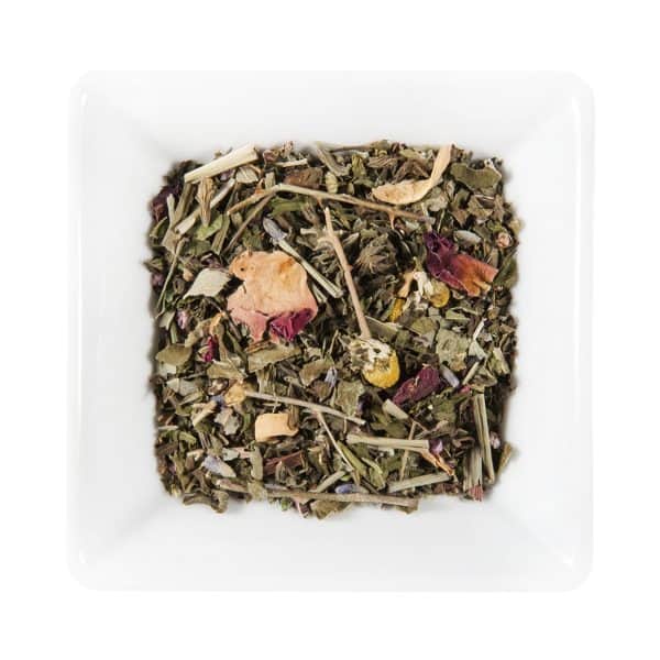 Бяла квадратна чиния, пълна с насипен билков чай, съдържащ зелени листа, сушени цветя и други естествени съставки, седи в топлата светлина на Залез Слънце.