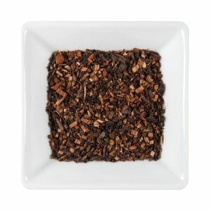 Бяла квадратна купа, пълна с насипни, изсушени листенца чай ройбос Хънибуш - Меден Храст Органик, погледнати отгоре на бял фон.