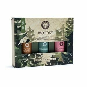 A Комплект за ароматерапия с етерични масла Woodsy, включващ три бутилки по 5 ml, надписани „In the Woods“, „Cedarwood“ и „Frankincense“. Кутията с горски дизайн е идеална за ароматерапия, а на нея пише 100% Pure.
