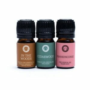 Три кафяви бутилки с етерично масло с надписи „In The Woods“, „Cedarwood“ и „Frankincense“ с черни капачки, подредени в редица – етерични масла, идеални за вашия Комплект за ароматерапия с етерични масла Woodsy.