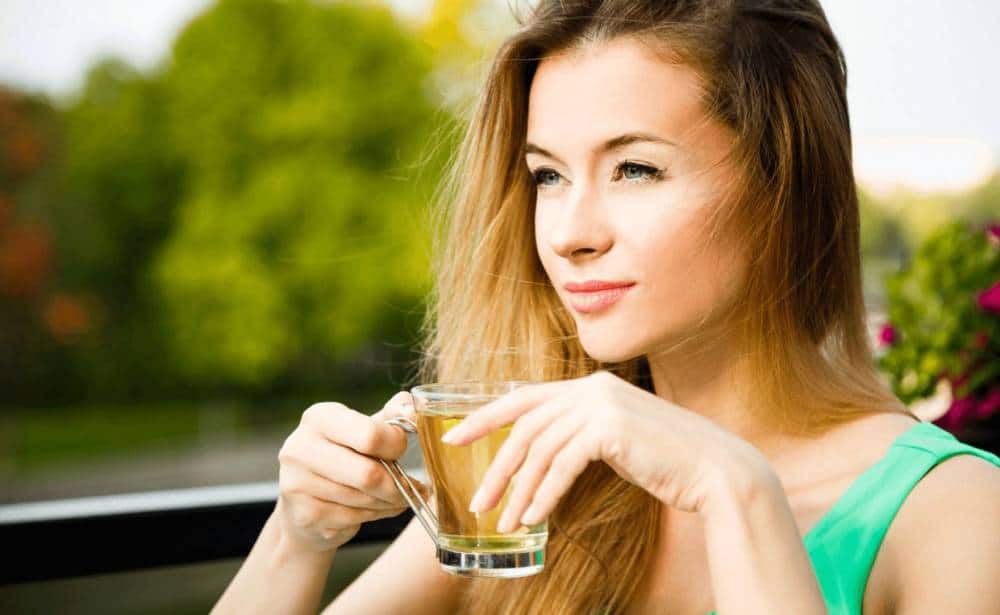 Жена пие зелен чай на балкон.