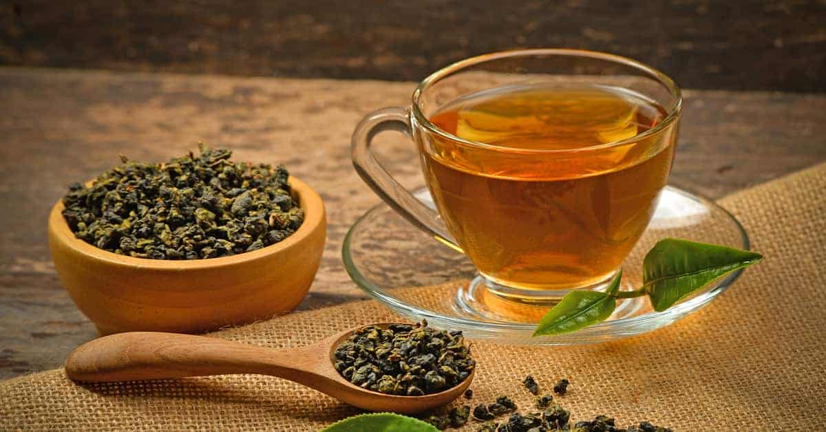 Чаша зелен чай с листа и лъжица.