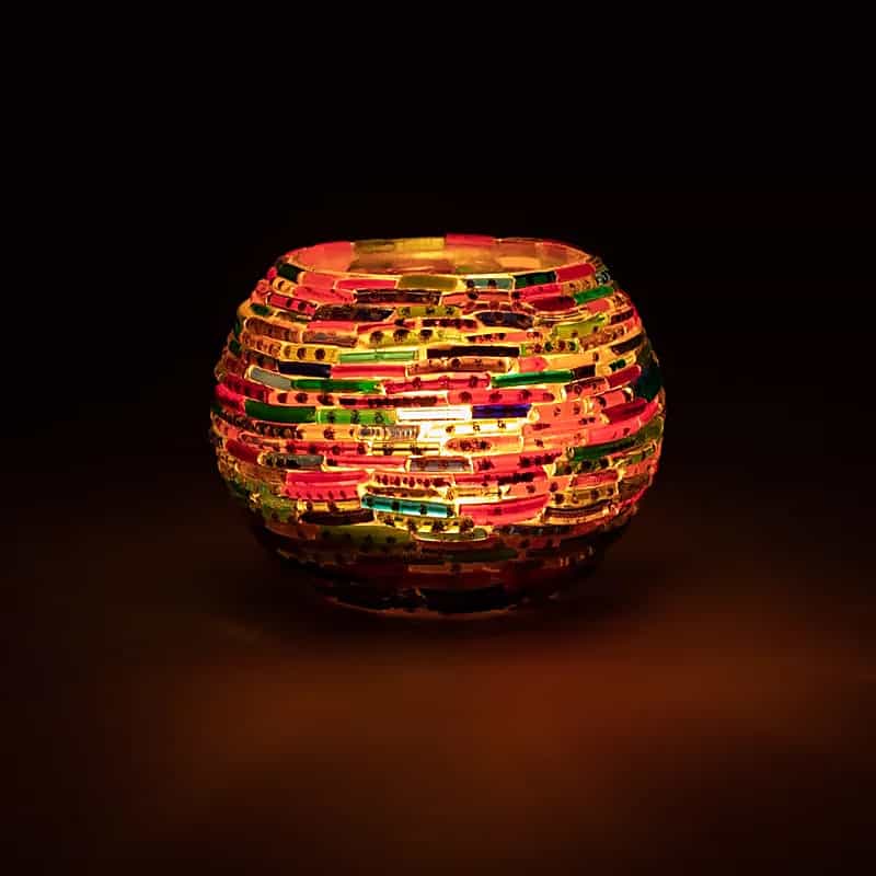 A colorful Мозаечен стъклен свещник Ленти lantern sitting on a dark table.