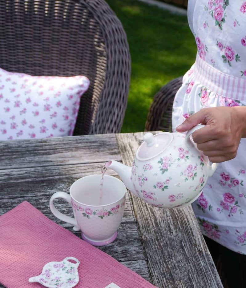 Жена на име Луси в розова престилка налива чай в Чайник Люси.